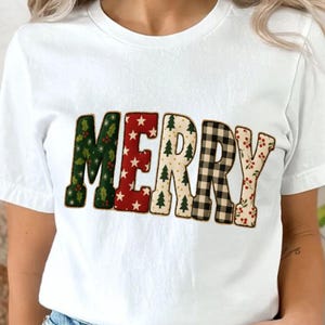 Pode incluir: Camiseta branca com a palavra "MERRY" em um design festivo. As letras são decoradas com padrões natalinos: azevinho verde, estrelas vermelhas, árvores de Natal, xadrez preto e branco e bagas vermelhas.
