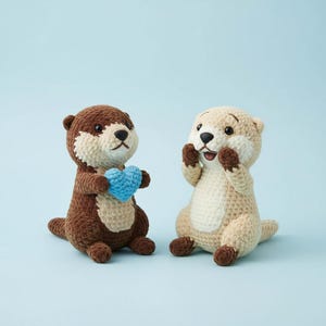 May include: Two crocheted otter plushies. One is brown and holding a blue heart. The other is tan with brown accents, hands raised. Both have black eyes and white faces. Set against a light blue background.
