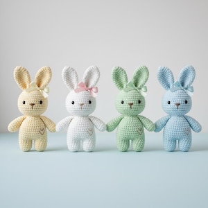 May include: Four crocheted bunny dolls in pastel colors: yellow, white, green, and blue. Each bunny has long ears, a small bow, and a heart detail. The dolls are handmade and suitable for children.