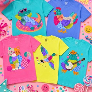 May include: A collection of colorful t-shirts with whimsical animal designs. The shirts feature a crocodile in a donut float, a chicken, a cat, a duck, and a frog playing a banjo. The text "OH HAPPY DAY" is visible.