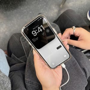 May include: A smartphone with a clear case displays the time as 9:41 on a black and white screen. The phone is connected to a white charging cable. The date is Wednesday, April 1.