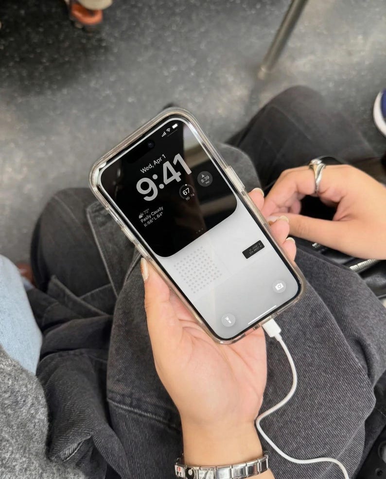 May include: A smartphone with a clear case displays the time as 9:41 on a black and white screen. The phone is connected to a white charging cable. The date is Wednesday, April 1.