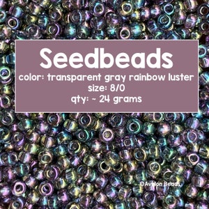 Pode incluir: Uma imagem de close-up de um monte de contas de sementes cinzas transparentes com um brilho arco-íris. As contas são de tamanho 8/0 e pesam aproximadamente 24 gramas. O texto "Seedbeads" está escrito em branco sobre um fundo roxo, juntamente com os detalhes "color: transparent gray rainbow luster", "size: 8/0", e "qty: ~ 24 grams".