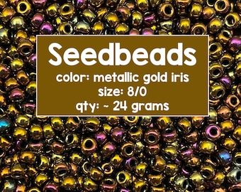 Puede incluir: Una imagen de primer plano de un montón de cuentas de semillas de iris dorado metálico, tamaño 8/0. Las cuentas pesan aproximadamente 24 gramos. El texto "Seedbeads" se muestra en letras blancas sobre un fondo marrón, junto con los detalles "color: metallic gold iris", "size: 8/0" y "qty: ~ 24 grams". El texto "Avalon Beads" se muestra en letras blancas sobre un fondo marrón.
