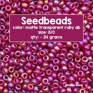 May include: A close-up image of a pile of 8/0 seed beads in a matte transparent ruby ab color. The beads are approximately 24 grams in weight. The text "Seedbeads" is displayed in a white font on a pink background. The text "color: matte transparent ruby ab" is displayed in white font on a pink background. The text "size: 8/0" is displayed in white font on a pink background. The text "qty: ~ 24 grams" is displayed in white font on a pink background. The text "Avalon Beads" is displayed in white font on a pink background.