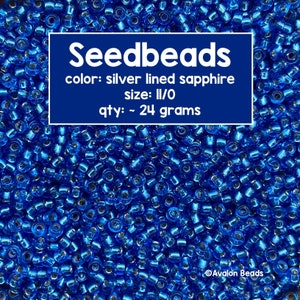 May include: A close-up image of a pile of blue seed beads with silver lining. The beads are size 11/0 and weigh approximately 24 grams. The text on the image reads "Seedbeads, color: silver lined sapphire, size: II/O, qty: ~ 24 grams, Avalon Beads".