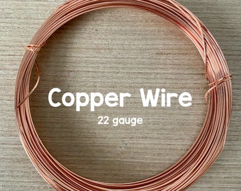 May include: Coiled copper wire, 22 gauge, displayed on a light wood surface. The text "Copper Wire" and "22 gauge" are visible in white. The wire is a warm, reddish-brown color.