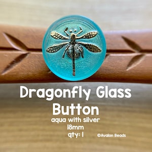 May include: Aqua blue glass button featuring a silver dragonfly design. The button measures 18mm in diameter. ©Avalon Beads