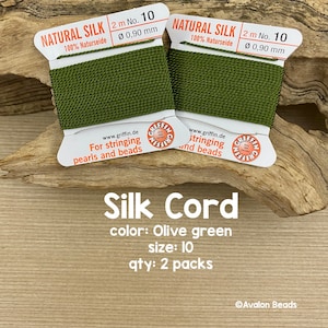 May include: Two spools of olive green natural silk cord, each 2 meters long and 0.90 mm in diameter. The spools are labeled "Natural Silk 100% Naturseide 2 m No. 10 Ø 0,90 mm" and "For stringing pearls and beads www.griffin.de".