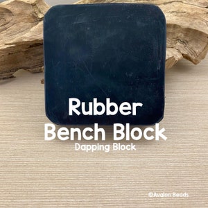 Könnte beinhalten: Ein schwarzer Gummi-Werkblock mit abgerundeten Ecken. Der Text "Rubber Bench Block Dapping Block" ist in Weiß dargestellt. Der Block befindet sich auf einer hellen Holzoberfläche.