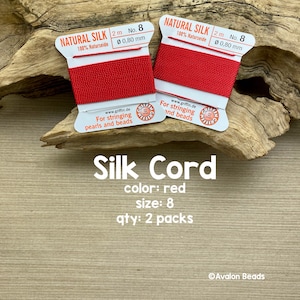 May include: Two spools of red natural silk cord, each 2 meters long and 0.80 mm thick. The spools are labeled "Natural Silk 100% Naturseide" and "For stringing pearls and beads".