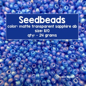 May include: A close-up of a pile of small, light blue seed beads. The beads are matte and transparent with a sapphire ab finish. The text on the image reads "Seedbeads", "color: matte transparent sapphire ab", "size: II/O", "qty: ~ 24 grams", and "Avalon Beads".
