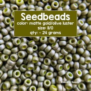 Pode incluir: Uma imagem de close-up de um monte de contas de sementes de ouro fosco e oliva lustroso. As contas são de tamanho II/O e pesam aproximadamente 24 gramas. O texto "Seedbeads" está escrito em letras brancas sobre um fundo verde. O texto "color: matte gold/olive luster", "size: II/O" e "qty: ~ 24 grams" também está escrito em letras brancas sobre um fundo verde.