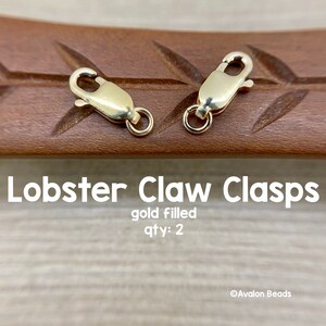 May include: Two gold-filled lobster claw clasps on a wooden surface.  gold filled qty: 2
