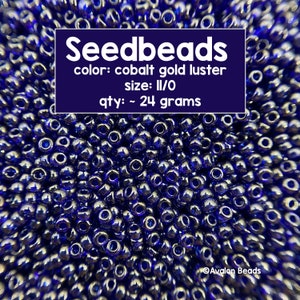 Pode incluir: Uma imagem de close-up de um monte de pequenas contas redondas de cor azul cobalto com um acabamento brilhante dourado. As contas são de tamanho 11/0 aproximadamente e pesam aproximadamente 24 gramas. O texto "Seedbeads" está escrito em letras brancas sobre um fundo roxo, juntamente com os detalhes "color: cobalt gold luster", "size: II/O" e "qty: ~ 24 grams".