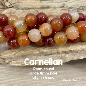 Könnte beinhalten: Eine Strang aus Karneolperlen, 12 mm rund mit einem großen 4 mm Loch. Die Perlen sind in einem Mix aus Orange, Rot und Braun.