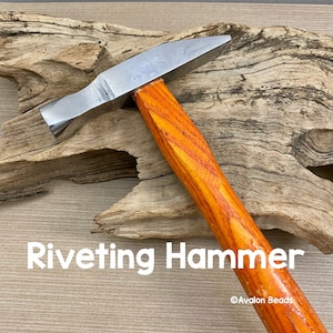 Puede incluir: Un martillo de ribeteado plateado con mango de madera naranja. El martillo está apoyado en un trozo de madera a la deriva. El texto "Riveting Hammer" está impreso debajo del martillo. El texto "Avalon Beads" está impreso en la esquina inferior derecha de la imagen.