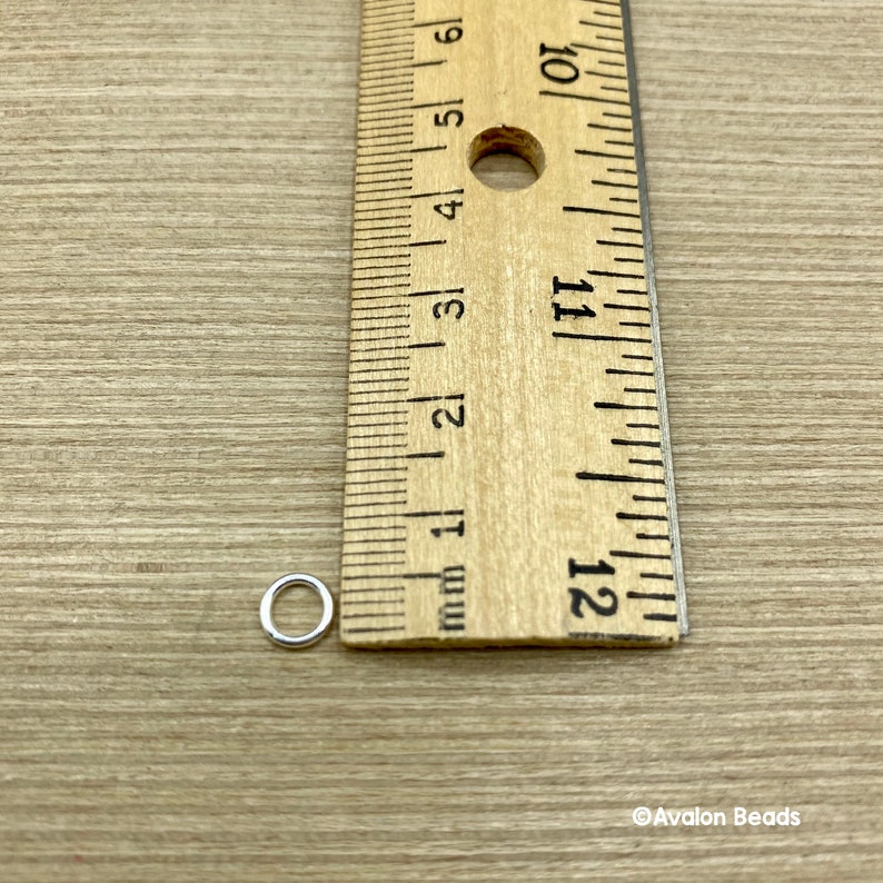 May include: A silver jump ring measuring approximately 6 mm in diameter, next to a ruler.
