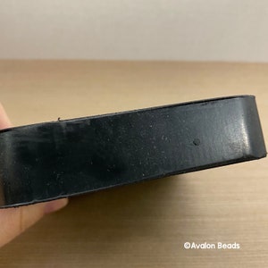 May include: A black, rectangular rubber object with rounded edges. The object appears to be a coaster or a similar protective item. The surface has a slightly textured appearance.