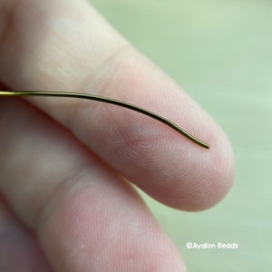 May include: A close-up of a thin, gold-colored wire bent into a slight curve. The wire is held between two fingers.