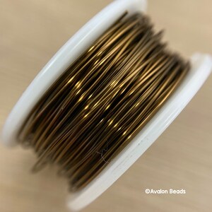 May include: A spool of gold-colored wire for jewelry making. The wire is wound tightly around a white plastic spool.