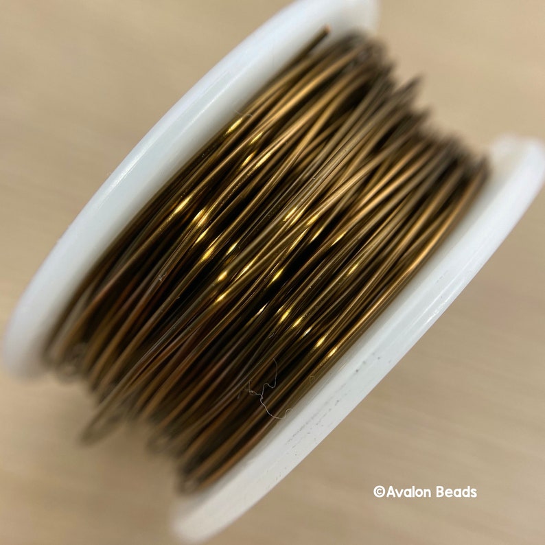 May include: A spool of gold-colored wire for jewelry making. The wire is wound tightly around a white plastic spool.