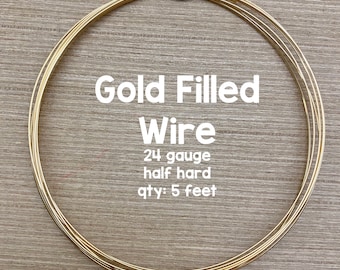 May include: A coil of gold filled wire, 24 gauge, half hard, 5 feet long. The wire is coiled in a circle and is on a wooden surface. The text "Gold Filled Wire" is written in white letters on a black background. The text "24 gauge half hard qty: 5 feet" is written in black letters on a white background.