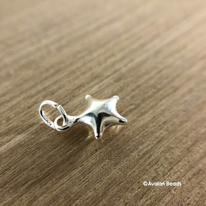 May include: A silver charm in the shape of a star with a loop for attaching to a bracelet or necklace.