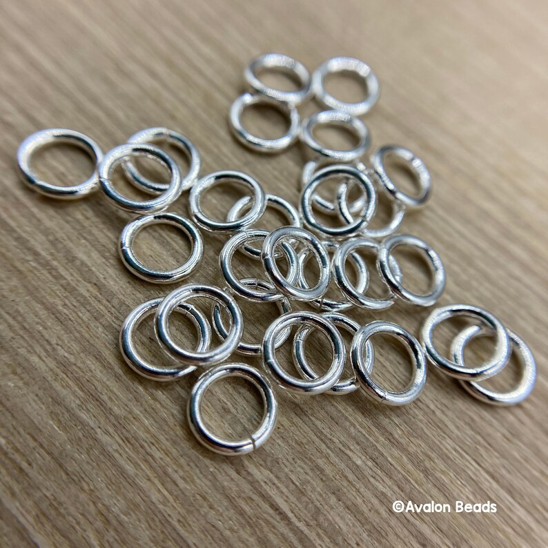 May include: A pile of silver jump rings, a type of jewelry finding used for connecting chains, cords, and other jewelry components.