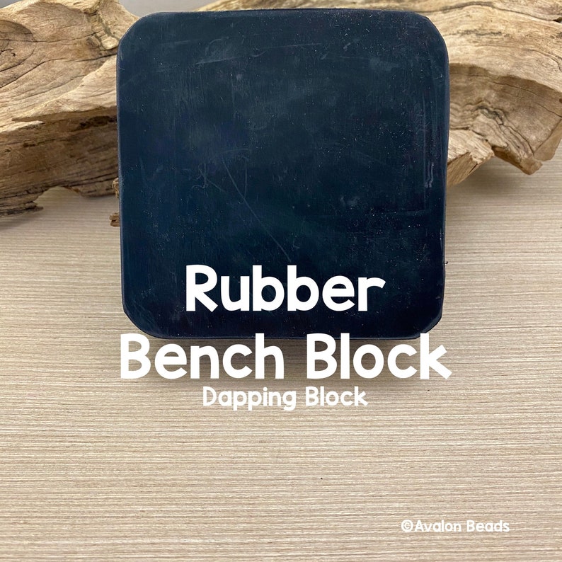 May include: A black rubber bench block with rounded corners. The text "Rubber Bench Block Dapping Block" is displayed in white. The block is on a light wood surface.