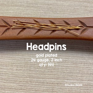 May include: Gold plated headpins, 24 gauge, 2 inches long, quantity 144. The headpins are arranged on a wooden surface.
