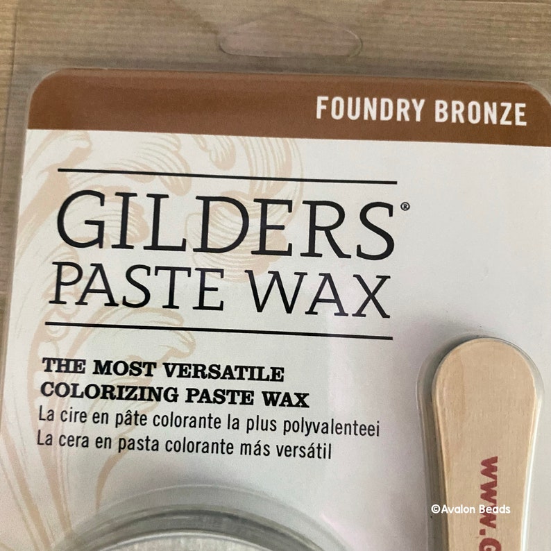 May include: A container of Foundry Bronze GILDERS PASTE WAX, a versatile coloring paste wax. The label reads "The Most Versatile Coloring Paste Wax" and includes French and Spanish translations. The container is accompanied by a wooden applicator.