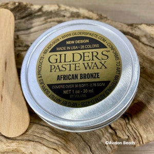 Pode incluir: Uma lata redonda de metal com um r&oacute;tulo dourado que diz "GILDERS PASTE WAX AFRICAN BRONZE". O r&oacute;tulo tamb&eacute;m diz "Novo design, Feito nos EUA, 28 cores, Cobre mais de 30 p&eacute;s quadrados - 2,78 metros quadrados, Conte&uacute;do l&iacute;quido 1 oz - 30 ml por volume".