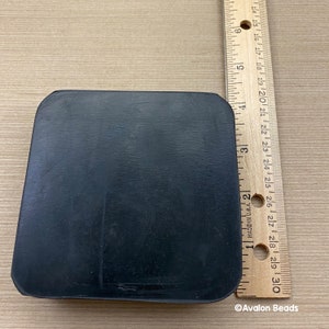May include: A black, rectangular object with rounded corners, possibly a base or pad. A wooden ruler with inch markings is next to the object. The ruler shows measurements up to 30 cm. The object's surface appears smooth.