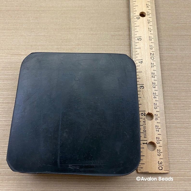 May include: A black, rectangular object with rounded corners, possibly a base or pad. A wooden ruler with inch markings is next to the object. The ruler shows measurements up to 30 cm. The object's surface appears smooth.
