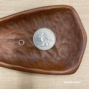 May include: A silver jump ring next to a US quarter dollar coin. The jump ring is a small, circular piece of metal with a gap in it. It is used for connecting jewelry pieces together.