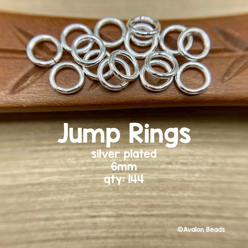 May include: A close-up of 144 silver-plated jump rings, each measuring 6mm in diameter. The rings are scattered on a wooden surface.