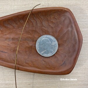 May include: A gold-colored wire is lying on a wooden tray. A US quarter is also on the tray. The quarter has the words "United States of America" and "Liberty" on it.