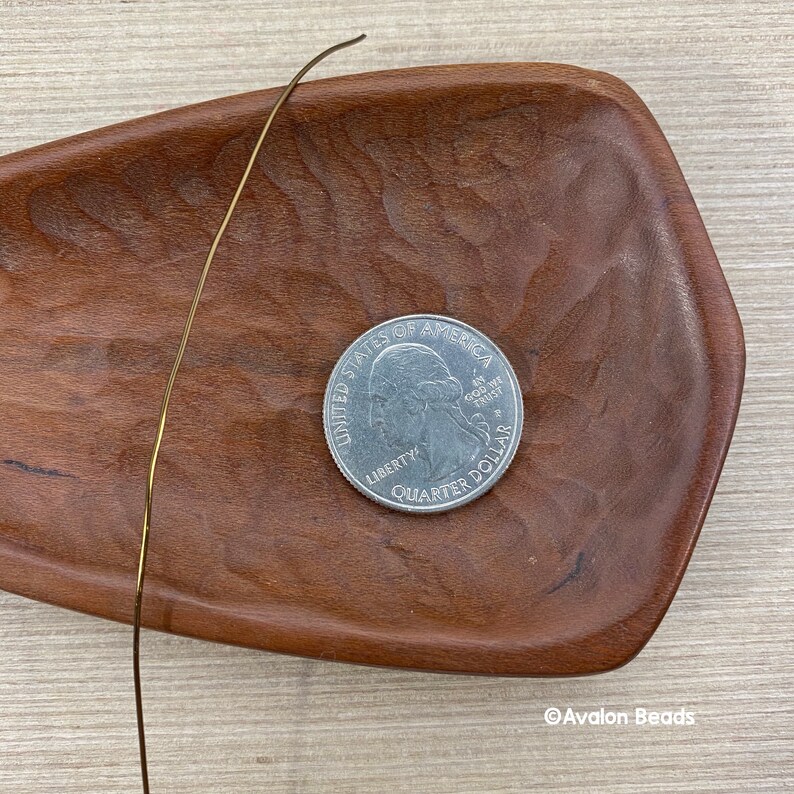 May include: A gold-colored wire is lying on a wooden tray. A US quarter is also on the tray. The quarter has the words "United States of America" and "Liberty" on it.