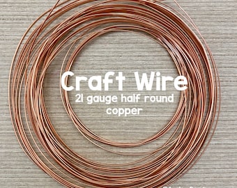May include: Coiled copper craft wire, 21 gauge half round. The wire is a warm, reddish-brown color and is arranged in a circular pattern. The text "Craft Wire" is displayed in white, along with the wire's specifications.