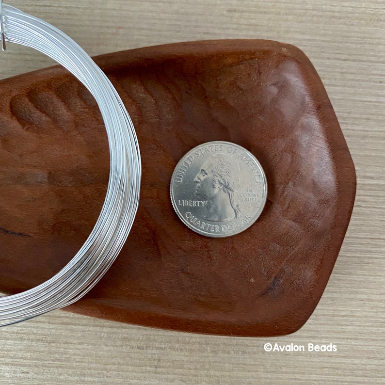 Puede incluir: Un rollo de alambre plateado, aproximadamente del tama&ntilde;o de una moneda de 25 centavos de d&oacute;lar estadounidense, sobre una superficie de madera.