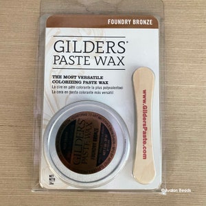 May include: A round tin of Gilders Paste Wax in Foundry Bronze. The tin is labeled with the product name, color, and website address. The tin is packaged with a wooden applicator stick.