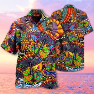 Puede incluir: Camisa de manga corta con un diseño psicodélico vibrante. La camisa presenta un colorido patrón de setas, caras y formas abstractas en tonos de azul, naranja, verde y morado. La palabra "Hippie" es visible en el cuello.