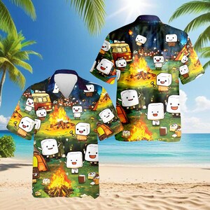 May include: Two short-sleeved Hawaiian shirts with a camping theme. The shirts feature a vibrant print of marshmallow characters around a campfire, with tents, a van, and a beach backdrop. The design includes a dark blue collar and a button-down front.