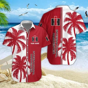Puede incluir: Camisa roja y blanca de manga corta con diseño de palmeras. La camisa presenta el logotipo y el texto de International Harvester. La camisa está en una playa con un océano azul y gaviotas en el fondo.