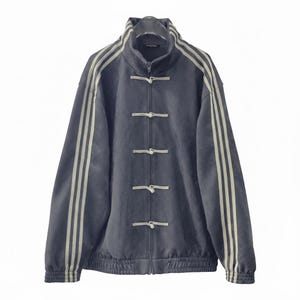 May include: A dark gray jacket with a high collar and a zipper closure. The jacket features three vertical stripes in a lighter color on each sleeve and decorative toggle closures down the front. The jacket has a ribbed hem and cuffs.