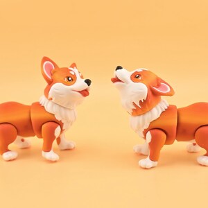 Pu&ograve; includere: Due statuette di cani corgi arancioni e bianchi con giunture articolate. Un cane guarda in alto con la bocca aperta, l'altro guarda avanti con la lingua di fuori. Le statuette hanno pelliccia bianca intorno al collo.
