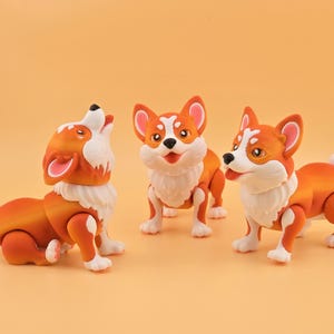 Pu&ograve; includere: Tre statuette di cani corgi arancioni e bianchi con arti articolati sono esposte su uno sfondo arancione pieno. Un cane ulula, un altro &egrave; in piedi e il terzo &egrave; a met&agrave; passo, tutti con accenti di pelliccia bianca.