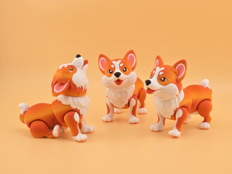 Pu&ograve; includere: Tre statuette di cani corgi arancioni e bianchi con arti articolati sono esposte su uno sfondo arancione pieno. Un cane ulula, un altro &egrave; in piedi e il terzo &egrave; a met&agrave; passo, tutti con accenti di pelliccia bianca.