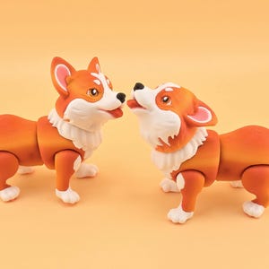 Pu&ograve; includere: Due statuette di cani corgi arancioni e bianchi. I cani hanno la pelliccia bianca intorno al collo e sulle zampe. Un cane guarda in alto con la lingua di fuori, e l'altro lo guarda. Lo sfondo &egrave; arancione chiaro uniforme.